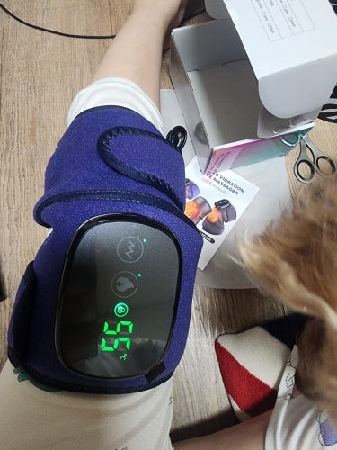 Person using a knee massager with digital controls displaying 55 degrees.