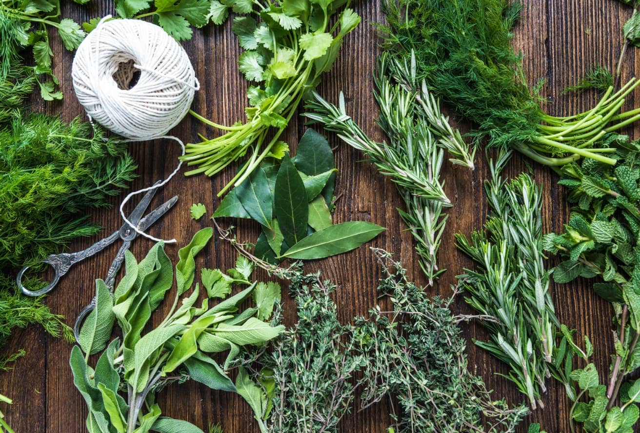 Various fresh herbs, scissors, and twine on a wooden surface.