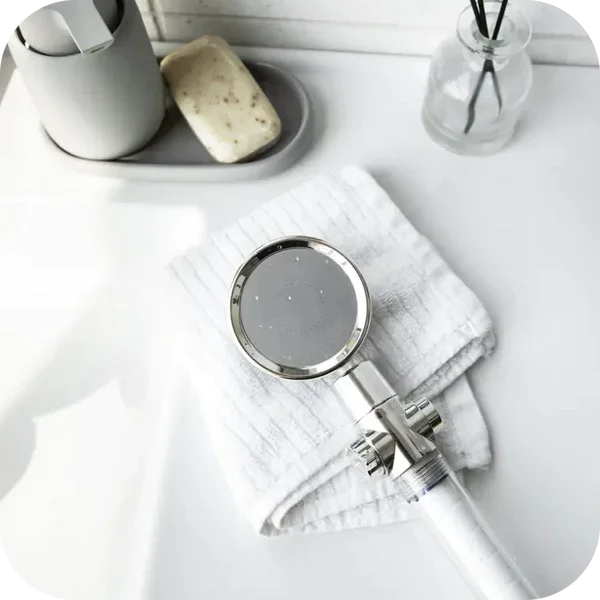 Showerhead on a folded towel beside soap and a jar on a white surface.