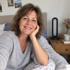 Une femme assise sur son lit, la lampe Solia posée sur la table de nuit.