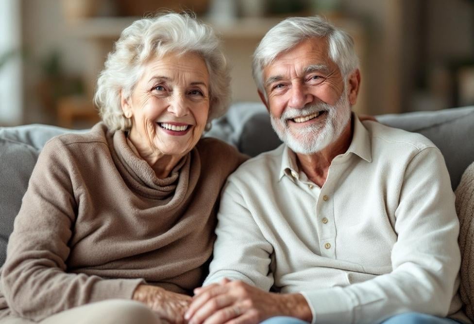 'Elderly couple smiling warmly while sitting on a sofa at home.'