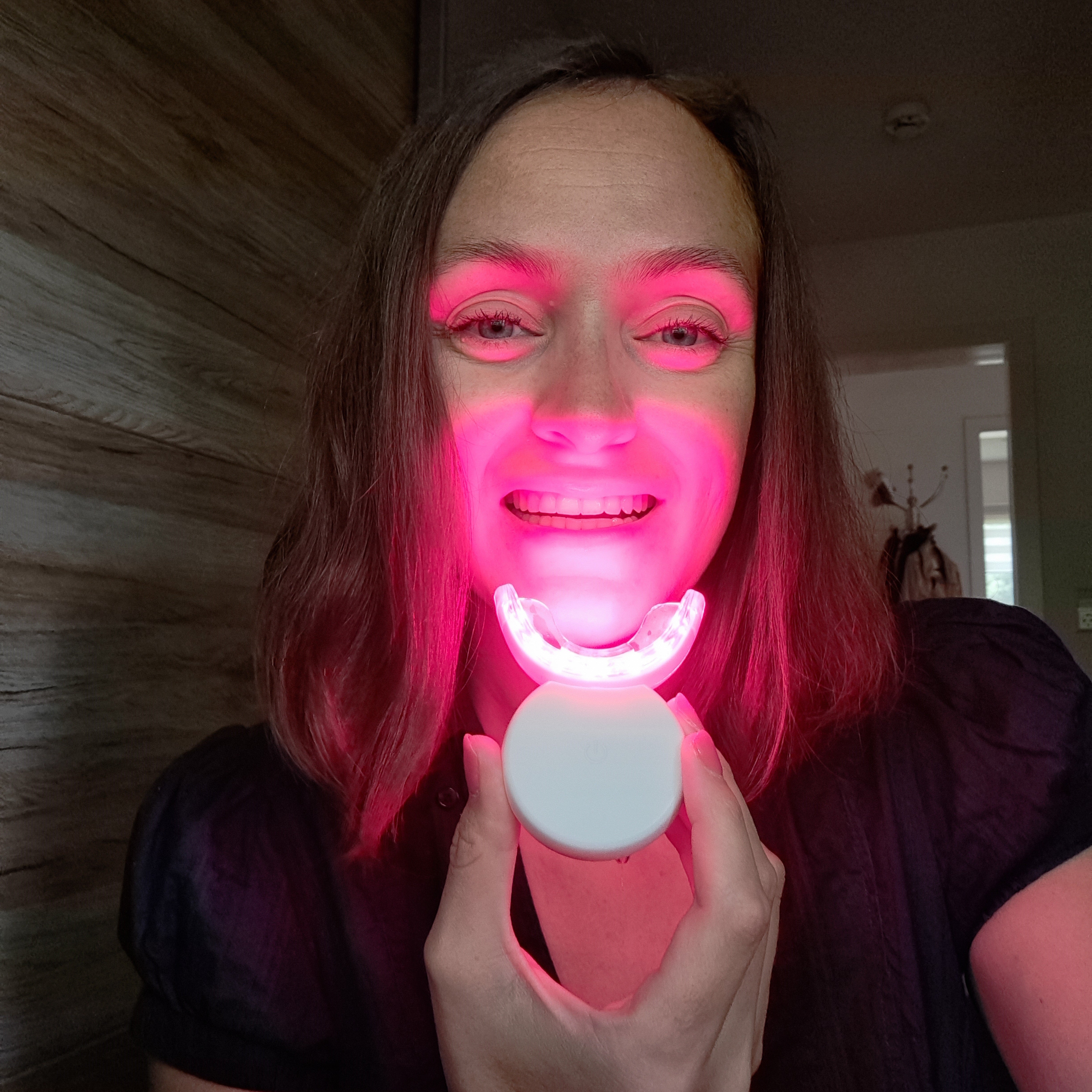Person using a glowing LED teeth whitening device.